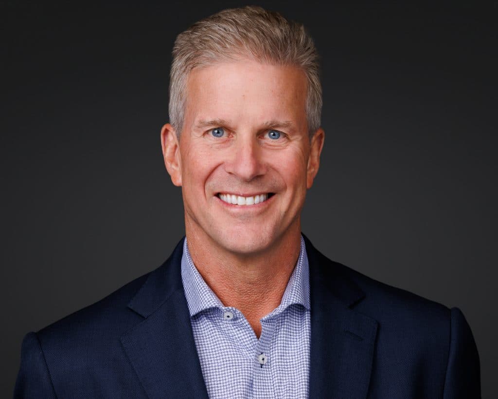 Smiling man with short gray hair wearing a dark suit jacket and checkered shirt poses for Chicago corporate headshot session