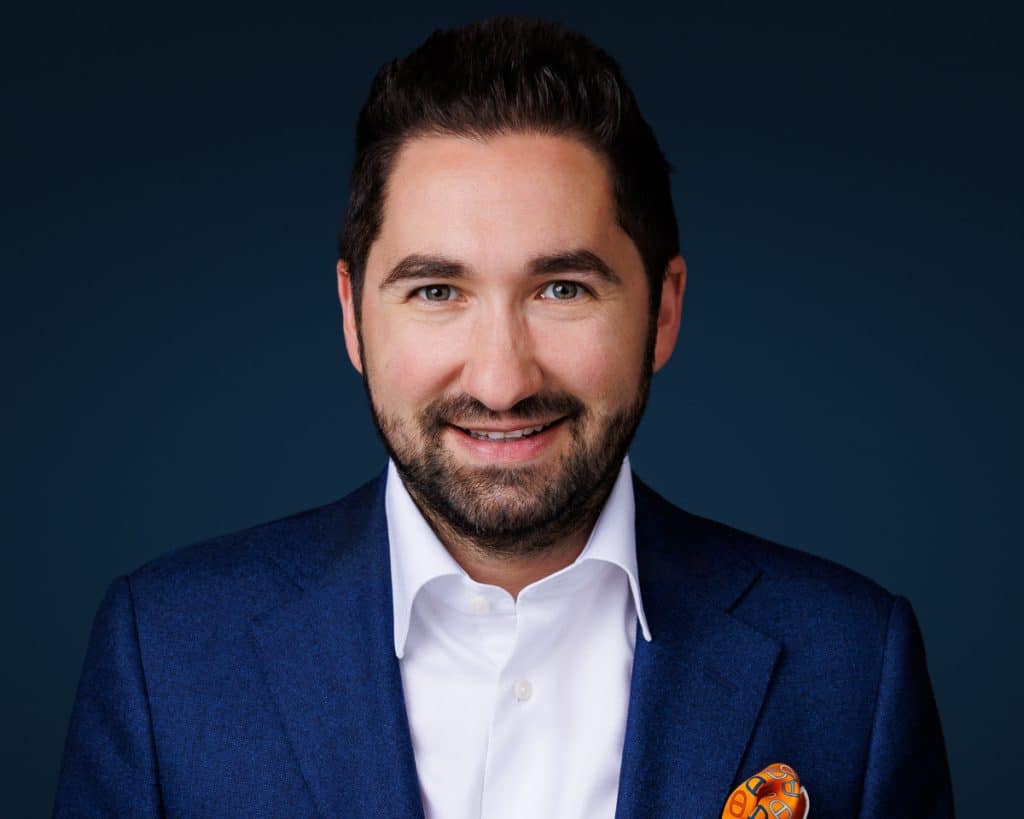 Business leadership headshot with a confident expression on a dark blue background