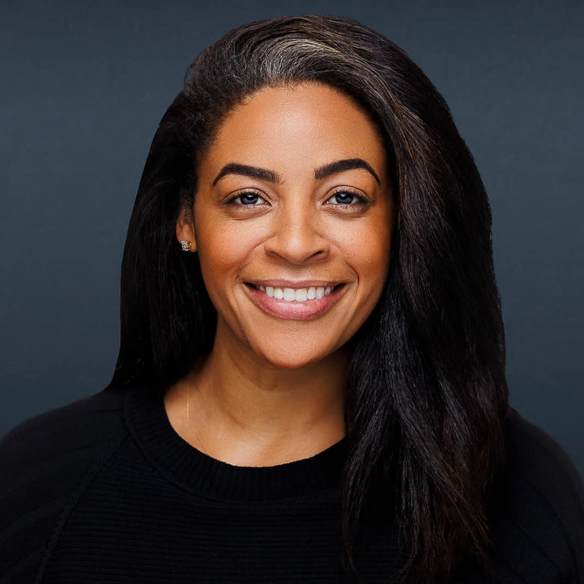 Chicago corporate headshot of a smiling woman with long dark hair, posed in front of a dark gray background