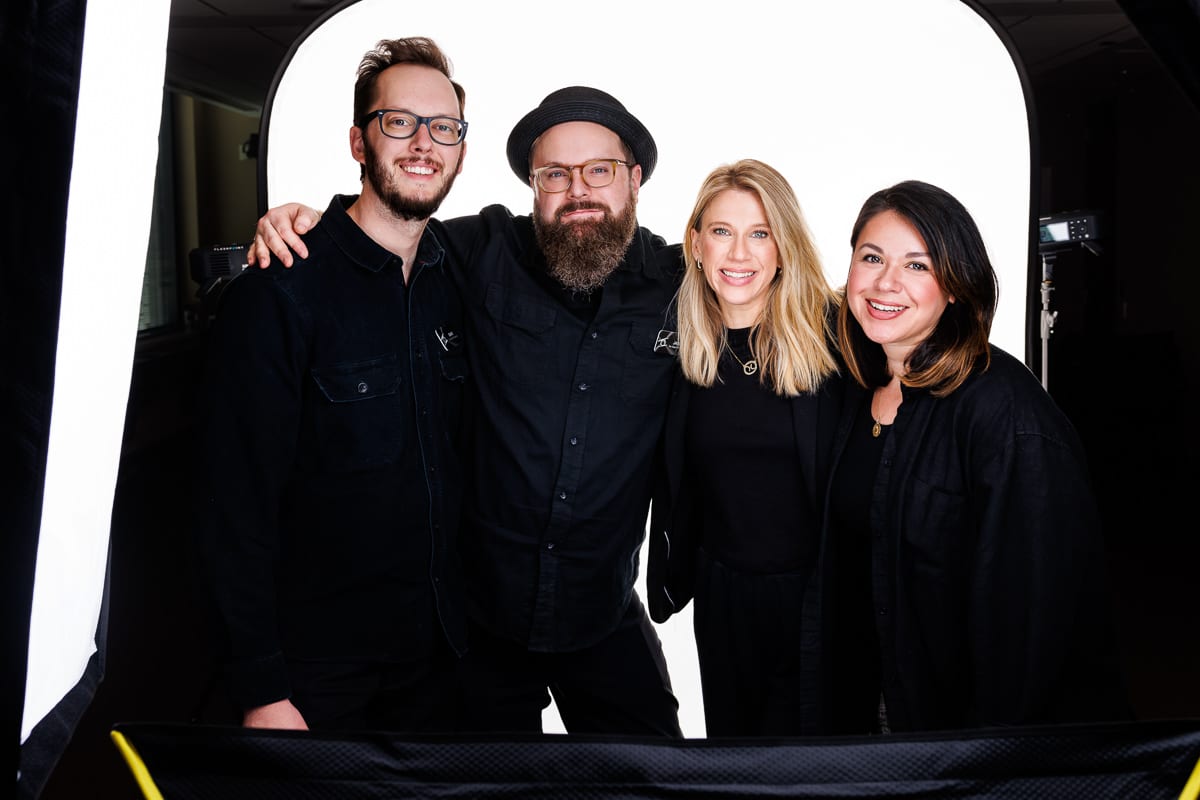 Commercial photography assistants posing together on set during a corporate headshot session, wearing professional black clothing in front of lighting equipment.