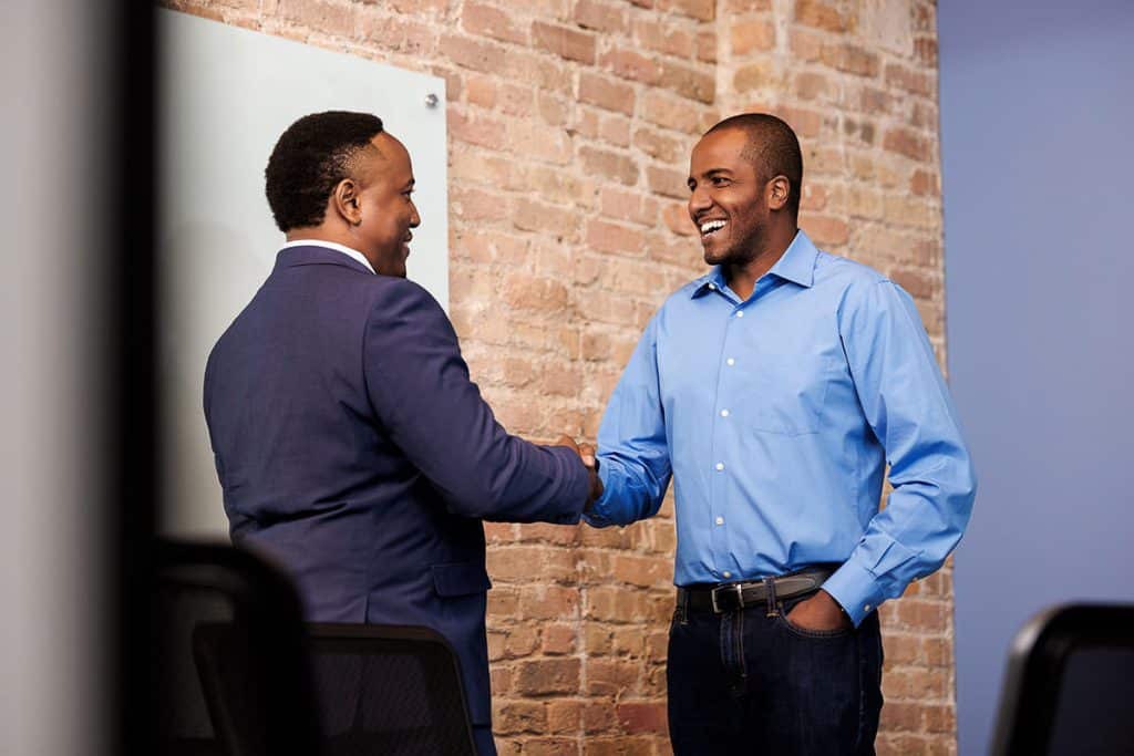 Two colleagues greeting each other during a conversation in a workplace setting, showing professional interaction and team rapport.