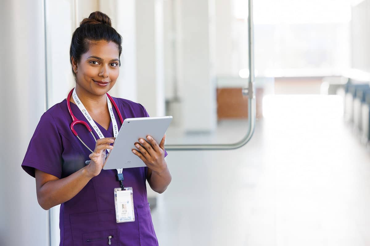 Healthcare professional using a tablet in a clinical setting, illustrating real people at work and modern workplace culture.