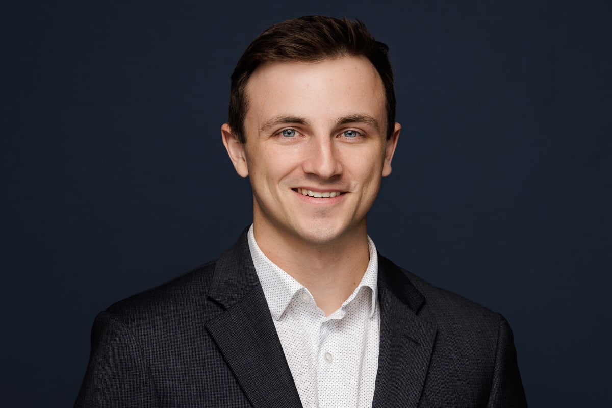 Young executive in a dark suit, smiling confidently, captured for Chicago corporate headshots by Tori Soper Photography.