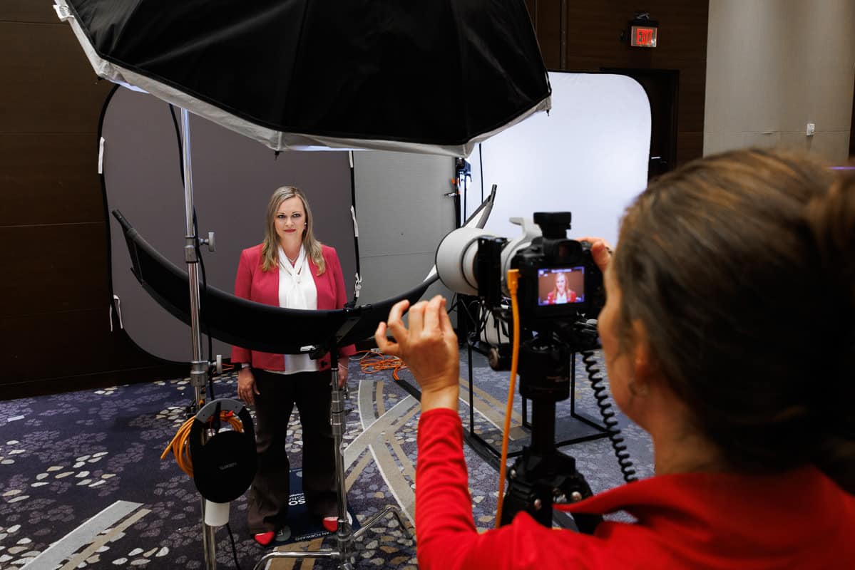 A woman in a red jacket stands poised in a photography studio setup, capturing the essence of Chicago professional headshots as another person takes her photo.